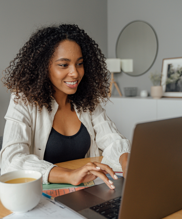 young lady at desk with tea working on laptop smiling